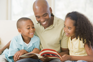 Man and two children sitting in living room reading book and smi