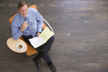 Wall Mural - Businessman sitting indoors with coffee and folder smiling