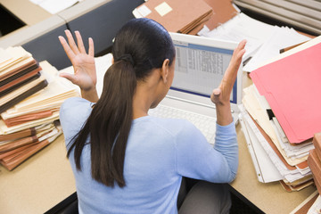 Wall Mural - Businesswoman in cubicle with laptop and stacks of files