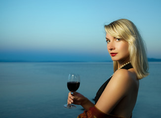 Canvas Print - Beautiful young woman drinks red wine near the ocean