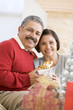 © Monkey Business - Middle Aged Couple Sitting On Sofa Holding Christmas Present