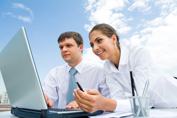 Sticker - Two successful co-workers sitting in front of laptop outdoors