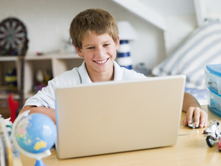 Young Boy Using A Laptop In His Bedroom