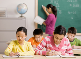 Concentrating students writing in notebook in school classroom
