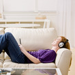 © AVAVA - Woman laying on sofa and listening to music on headphones