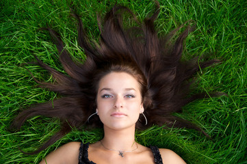 young nice girl lying on the green grass with brown hair