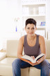 © nyul - Young woman reading book at home, sitting on sofa.
