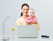 © AVAVA - Working mother holding baby while typing on laptop at desk