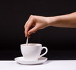 woman stir sugar in cup of coffee over black background