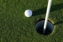 A White Golf Ball Near The Hole Of A Golfing Green Or Course