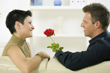 Wall Mural - Romantic man giving red rose to woman at home, smiling.