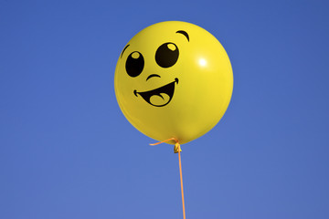 Smiling yellow balloon on blue sky background