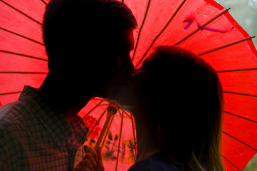 Silhouette of couple kissing in front of a red umbrella