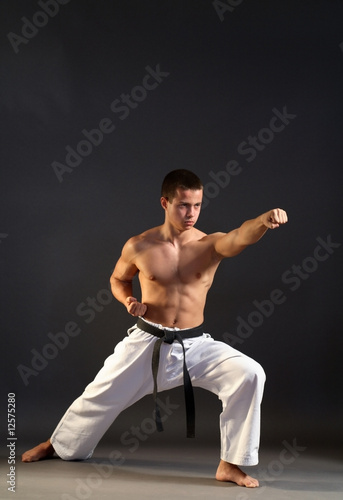 Board z aluminiowym obramowaniem Młody człowiek sportowy karate robi specjalne ćwiczenia na szary deseń