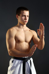 Young sporty karate man doing special exercise on gray backgroun