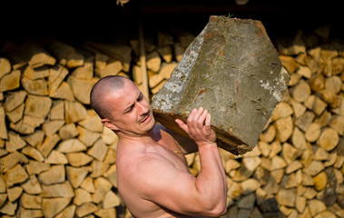 Strong man lifting a huge log, outdoor scene