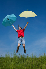 Girl holding umbrella jumping against blue sky