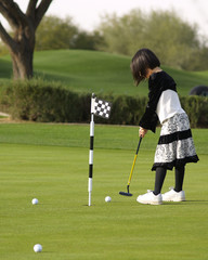 A young girl has fun playing golf on a beautiful green.