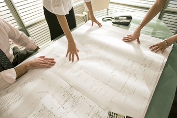 Closeup of professionals looking at architectural plans on desk