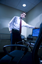 Young Businessman Next To Desk With Hand On Computer Monitor