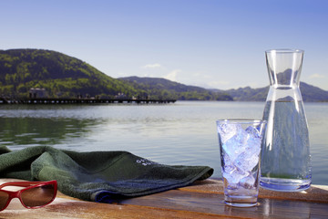 Glas Wasser mit Eiswürfel, Handtuch, Sonnenbrille und Krug am St