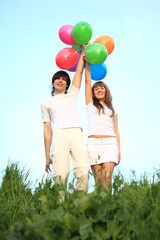 girl and guy stand in grass with multicoloured balloons over hea