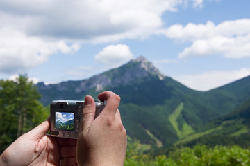 Hand with digital camera and shot of summer mountain