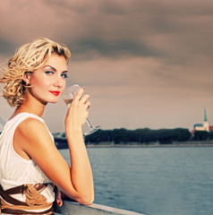 Wall Mural - Beautiful blond girl drinks champagne near the river