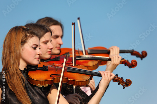 Cuadros en Lienzo trio of violinists plays against sky