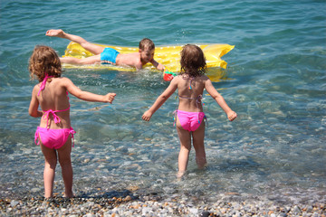 boy on inflatable mattress in sea and two girls nearby