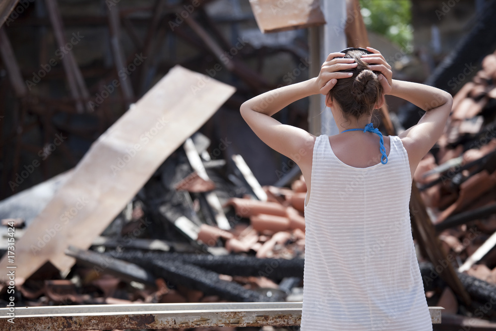 woman stands in front of burned out house - obrazy, fototapety, plakaty 