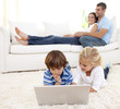 © WavebreakMediaMicro - Children using a laptop and parents lying on sofa