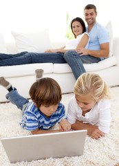 Wall Mural - Children using a laptop and couple lying on sofa