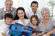 © WavebreakMediaMicro - Portrait of family holding a guitar in living-room