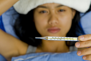 woman sick in bed with focus on thermometer