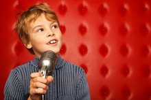 Portrait Of Boy With Microphone On Rack Against Red Wall