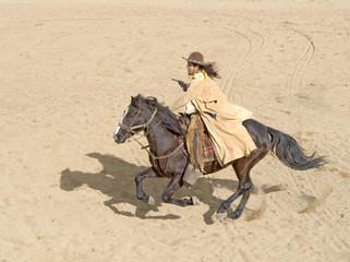 Fototapete - Cowboy riding a horse at full gallop with gun in hand