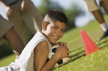 boy (13-15) lying down on grass holding soccer ball.