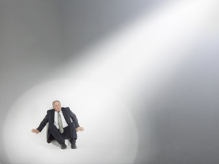 businessman sitting looking up at source of spotlight