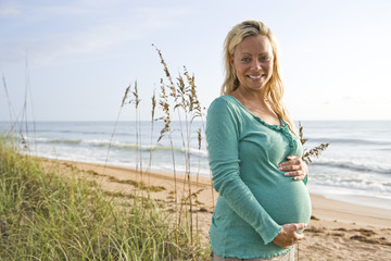 Happy young pregnant woman standing outdoors alone at beach