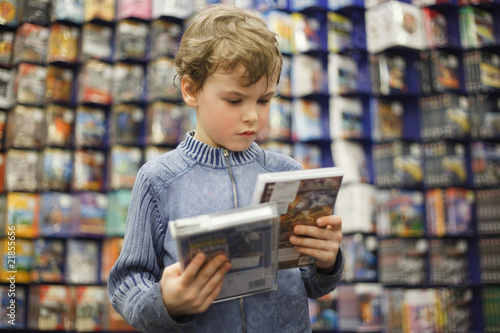 Fotografía boy chooses one of two dvd in special store, ready contents