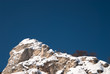 Snow-covered high rocky cliff against clear blue sky