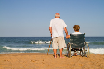 senior man and wheelchair wife on beach