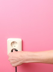 young woman's hand plugging a power plug into an electric wall s