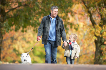 Man With Young Son Walking Dog Through Autumn Park