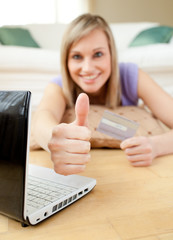 Wall Mural - Cheerful blond woman shopping on-line lying on the floor