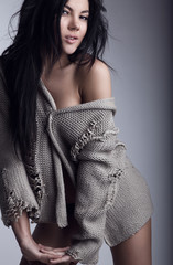 Beautiful young brunette in a woollen sweater pose on a grey bac