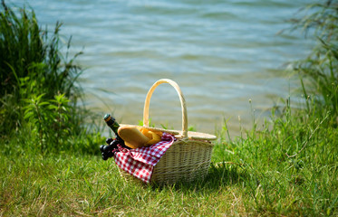 Picnic basket with food and cider bottle near the water