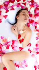 Attractive naked girl enjoys a bath with milk and rose petals