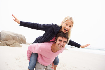 Wall Mural - Man Giving Woman Piggyback On Winter Beach